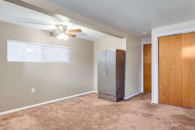 unfurnished bedroom featuring beam ceiling, ceiling fan, and light colored carpet