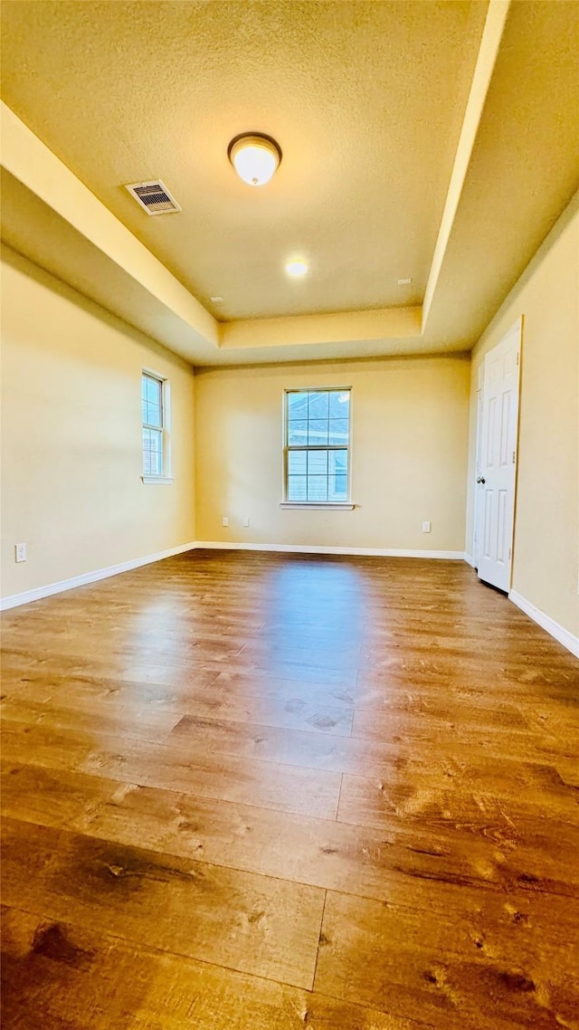 empty room featuring hardwood / wood-style floors, a textured ceiling, and a tray ceiling