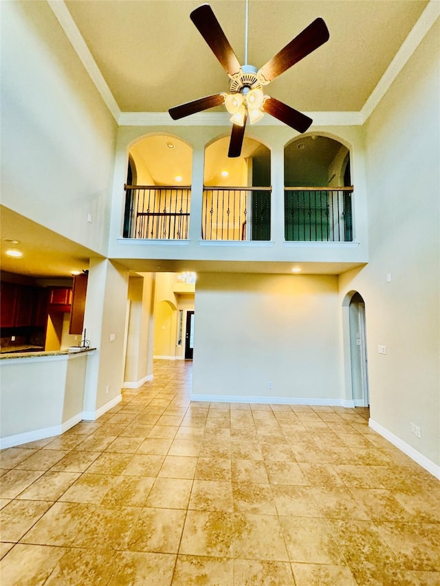 interior space with ceiling fan, ornamental molding, and a towering ceiling