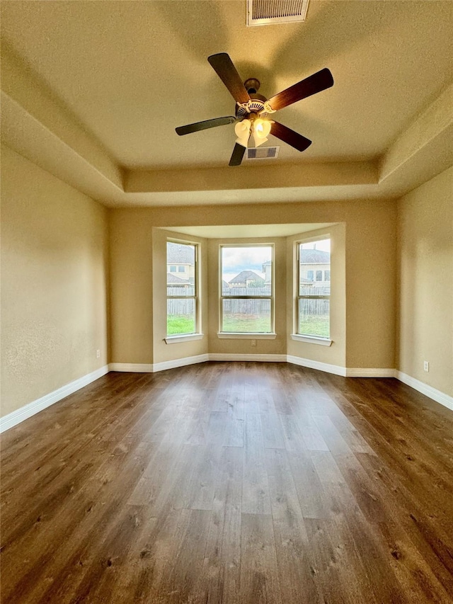 unfurnished room with a textured ceiling, ceiling fan, dark wood-type flooring, and a tray ceiling