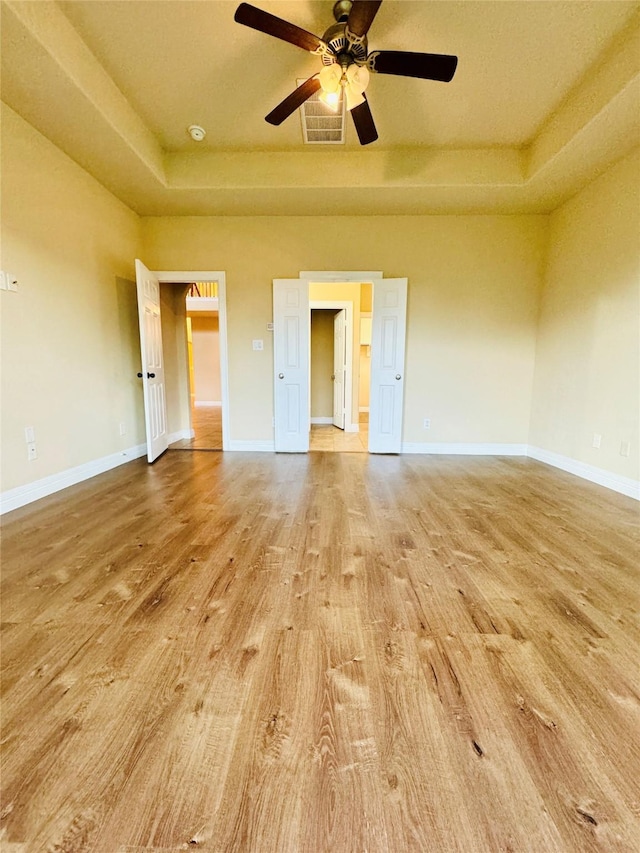 unfurnished room with a raised ceiling, ceiling fan, and light hardwood / wood-style floors