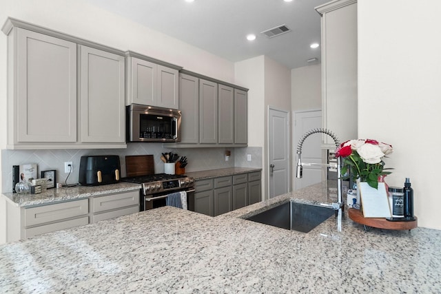 kitchen with gray cabinetry, light stone countertops, sink, stainless steel appliances, and tasteful backsplash