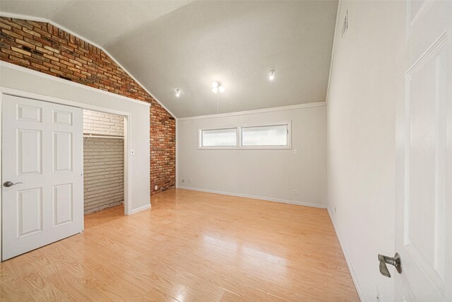 unfurnished bedroom with brick wall, vaulted ceiling, and light wood-type flooring