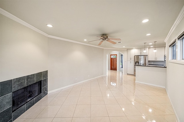 unfurnished living room with light tile patterned flooring, ceiling fan, ornamental molding, and a tiled fireplace