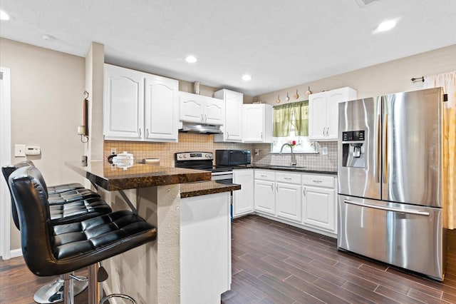 kitchen featuring kitchen peninsula, appliances with stainless steel finishes, dark wood-type flooring, sink, and white cabinets