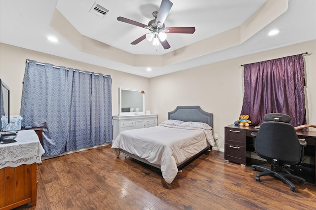 bedroom with dark hardwood / wood-style floors, ceiling fan, and a tray ceiling