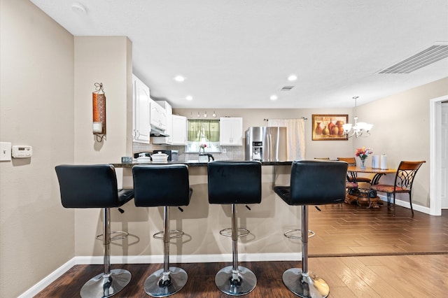 kitchen with white cabinets, kitchen peninsula, tasteful backsplash, dark hardwood / wood-style flooring, and stainless steel fridge with ice dispenser