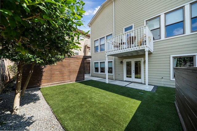 rear view of house with a lawn, a balcony, and french doors