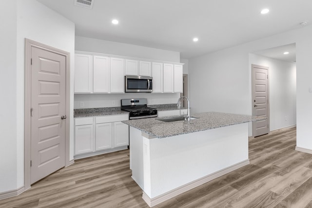 kitchen featuring appliances with stainless steel finishes, visible vents, a sink, light wood-style floors, and an island with sink