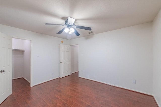 unfurnished bedroom featuring a closet, ceiling fan, dark hardwood / wood-style flooring, and a spacious closet