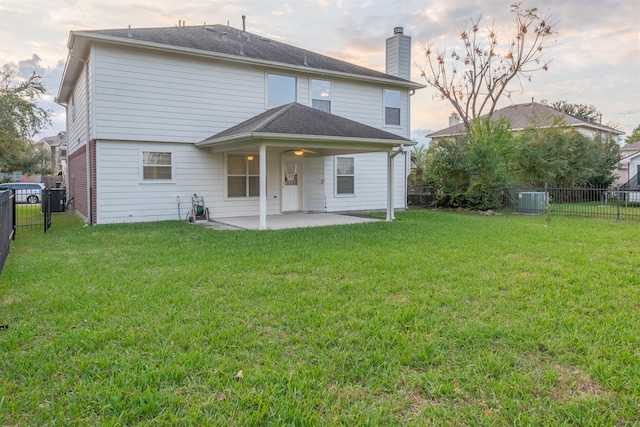 back house at dusk featuring central AC unit, ceiling fan, a patio area, and a yard