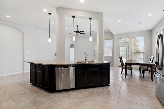 kitchen featuring pendant lighting, ceiling fan, an island with sink, light stone counters, and stainless steel appliances