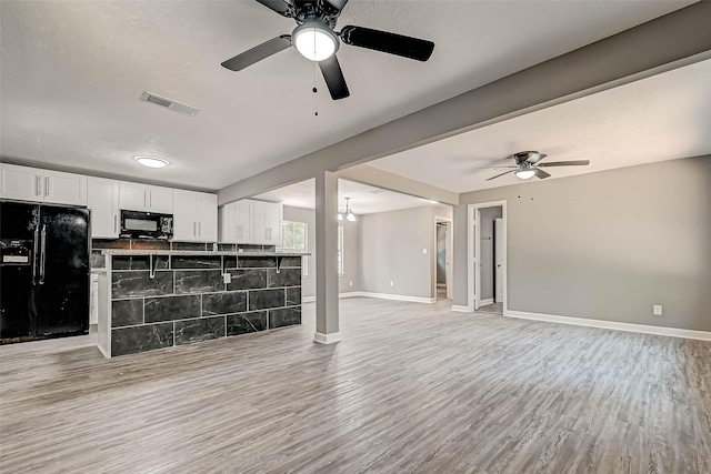 unfurnished living room with ceiling fan with notable chandelier, light hardwood / wood-style floors, and tile walls