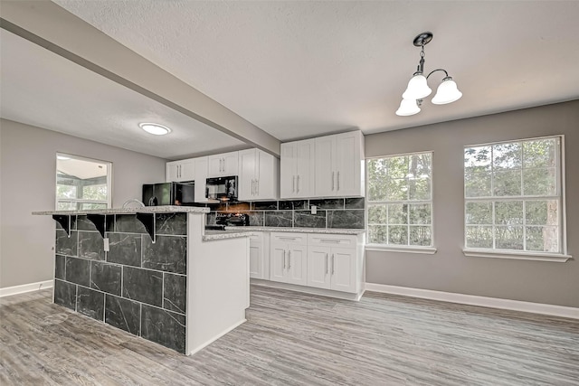 kitchen featuring black appliances, white cabinetry, hanging light fixtures, and light hardwood / wood-style flooring