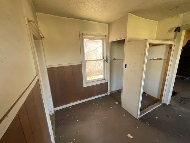 unfurnished bedroom featuring a textured ceiling, wooden walls, and a closet