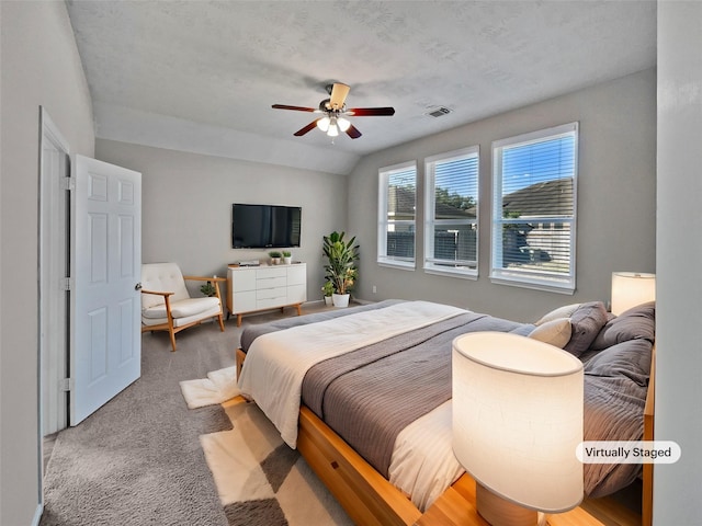 carpeted bedroom with a textured ceiling, vaulted ceiling, and ceiling fan