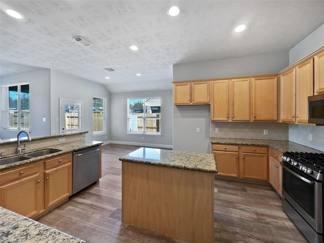 kitchen featuring hardwood / wood-style floors, a center island, sink, light stone counters, and stainless steel appliances