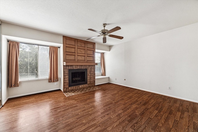 unfurnished living room with a fireplace, ceiling fan, dark hardwood / wood-style flooring, and a textured ceiling