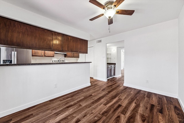 kitchen with dark wood-type flooring, kitchen peninsula, stainless steel refrigerator with ice dispenser, ceiling fan, and dark brown cabinetry