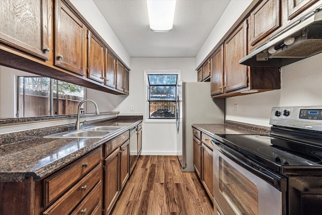 kitchen with appliances with stainless steel finishes, dark hardwood / wood-style flooring, dark brown cabinetry, and sink