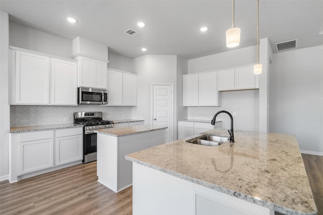 kitchen with a kitchen island with sink, sink, white cabinets, and appliances with stainless steel finishes