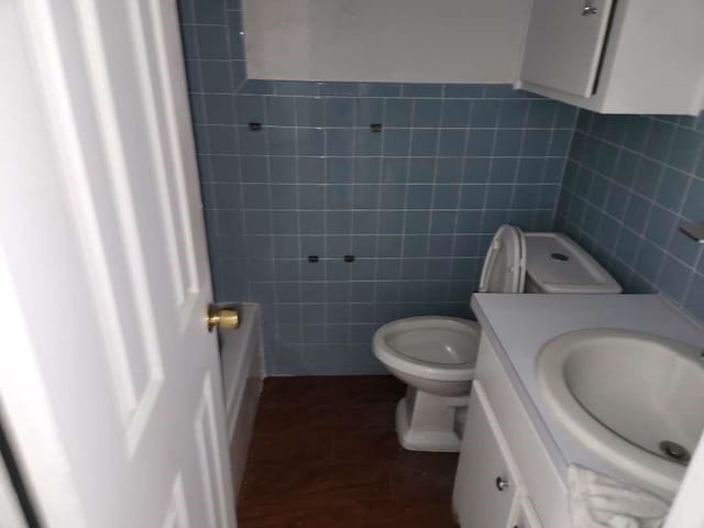 bathroom with a tub to relax in, vanity, tile walls, and toilet