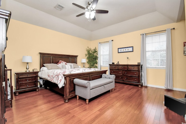 bedroom with ceiling fan, dark hardwood / wood-style flooring, and a tray ceiling