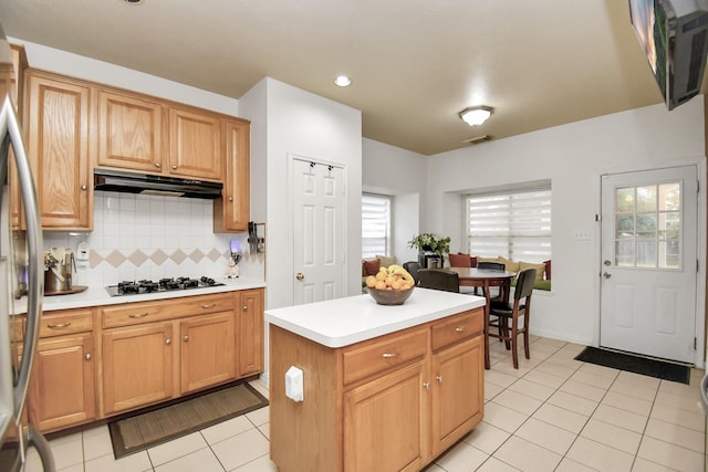 kitchen with stainless steel refrigerator, gas stovetop, light tile patterned flooring, backsplash, and a kitchen island