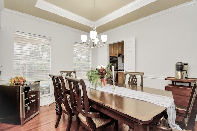 dining space with light hardwood / wood-style floors, crown molding, a tray ceiling, and a chandelier