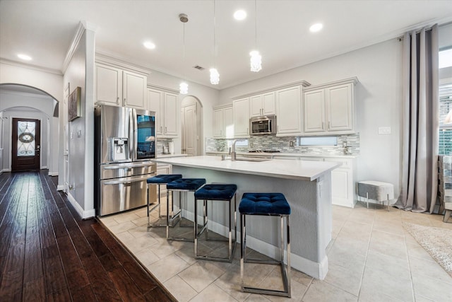 kitchen featuring pendant lighting, a kitchen island with sink, light hardwood / wood-style flooring, a kitchen bar, and stainless steel appliances