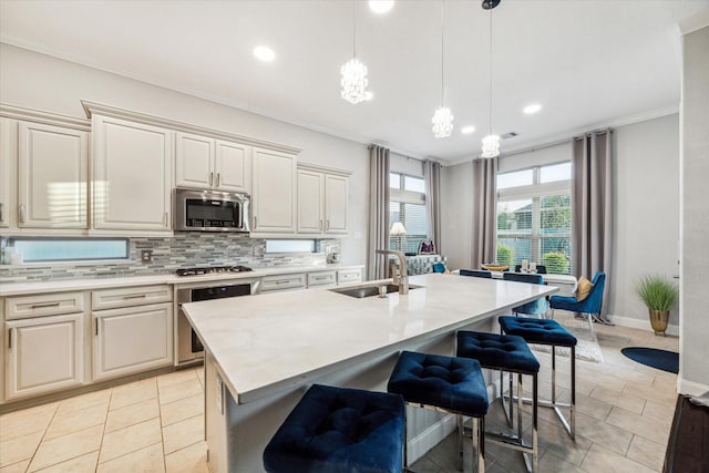 kitchen with a center island with sink, hanging light fixtures, light stone countertops, ornamental molding, and appliances with stainless steel finishes