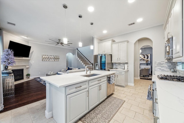 kitchen featuring ceiling fan, stainless steel appliances, decorative backsplash, a center island with sink, and white cabinets