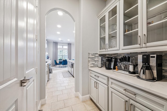 bar featuring white cabinets, decorative backsplash, light tile patterned floors, and light stone countertops