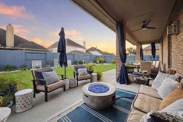 patio terrace at dusk featuring a lawn, ceiling fan, and an outdoor living space with a fire pit