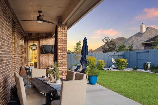 patio terrace at dusk featuring ceiling fan and a yard