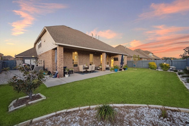 back house at dusk with a patio area and a lawn