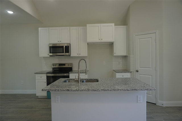 kitchen with light stone countertops, appliances with stainless steel finishes, sink, white cabinets, and an island with sink