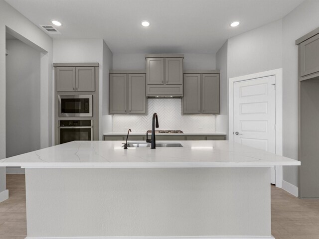 kitchen with light stone counters, sink, an island with sink, and stainless steel appliances