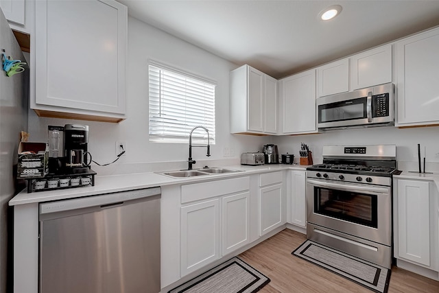 kitchen with sink, white cabinets, light hardwood / wood-style flooring, and appliances with stainless steel finishes