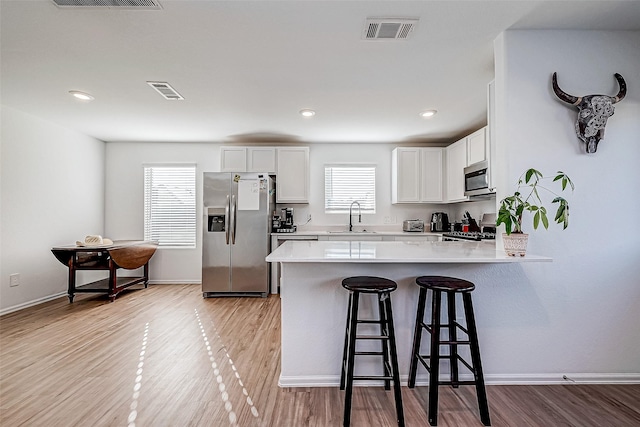 kitchen with white cabinets, a kitchen breakfast bar, appliances with stainless steel finishes, light hardwood / wood-style floors, and kitchen peninsula