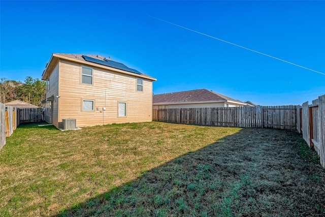 rear view of property with central AC unit, solar panels, and a yard