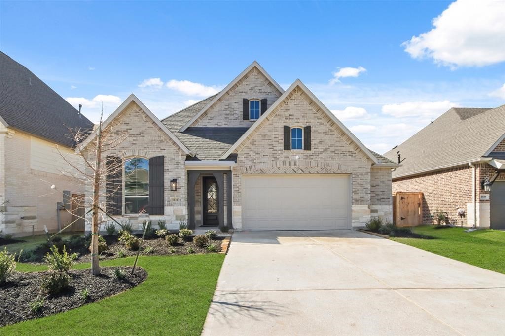 french country style house featuring brick siding, roof with shingles, a garage, driveway, and a front lawn