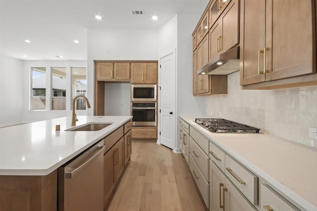 kitchen with a sink, under cabinet range hood, light wood-type flooring, visible vents, and appliances with stainless steel finishes