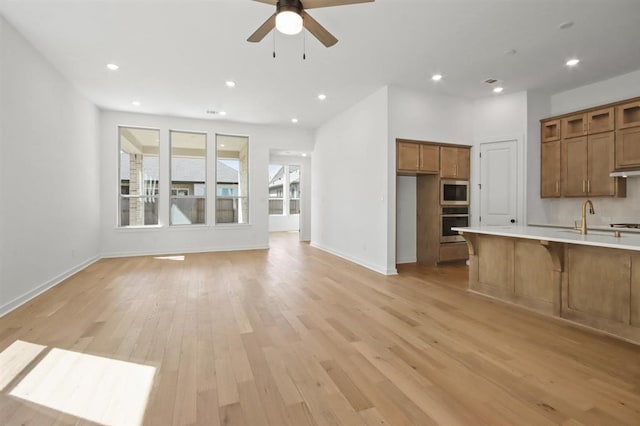 interior space featuring baseboards, ceiling fan, light wood finished floors, and a sink