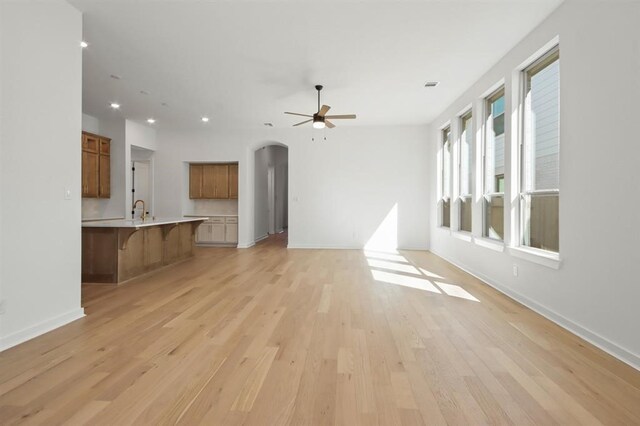 unfurnished living room with a sink, arched walkways, recessed lighting, light wood finished floors, and a ceiling fan