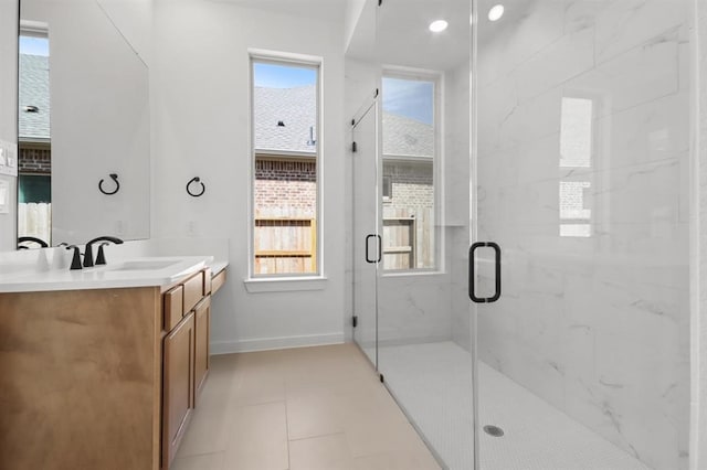 bathroom featuring a marble finish shower, baseboards, vanity, and a healthy amount of sunlight