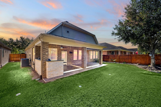 back house at dusk featuring a lawn and central AC unit