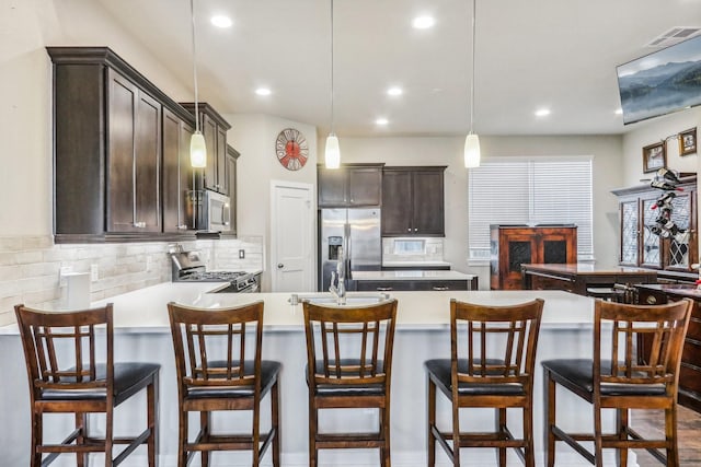 kitchen featuring dark brown cabinetry, stainless steel appliances, tasteful backsplash, decorative light fixtures, and a breakfast bar area