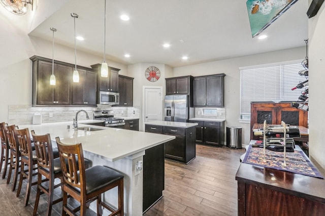 kitchen with appliances with stainless steel finishes, a kitchen breakfast bar, dark wood-type flooring, sink, and hanging light fixtures