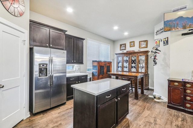 kitchen featuring stainless steel fridge with ice dispenser, light wood-type flooring, a center island, and dark brown cabinets